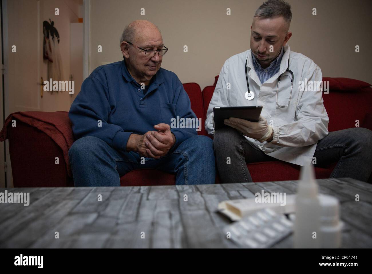 Ein Hausarzt und sein Patient zu Hause mit Medikamenten auf dem Tisch, Gesundheitspersonal. Stockfoto