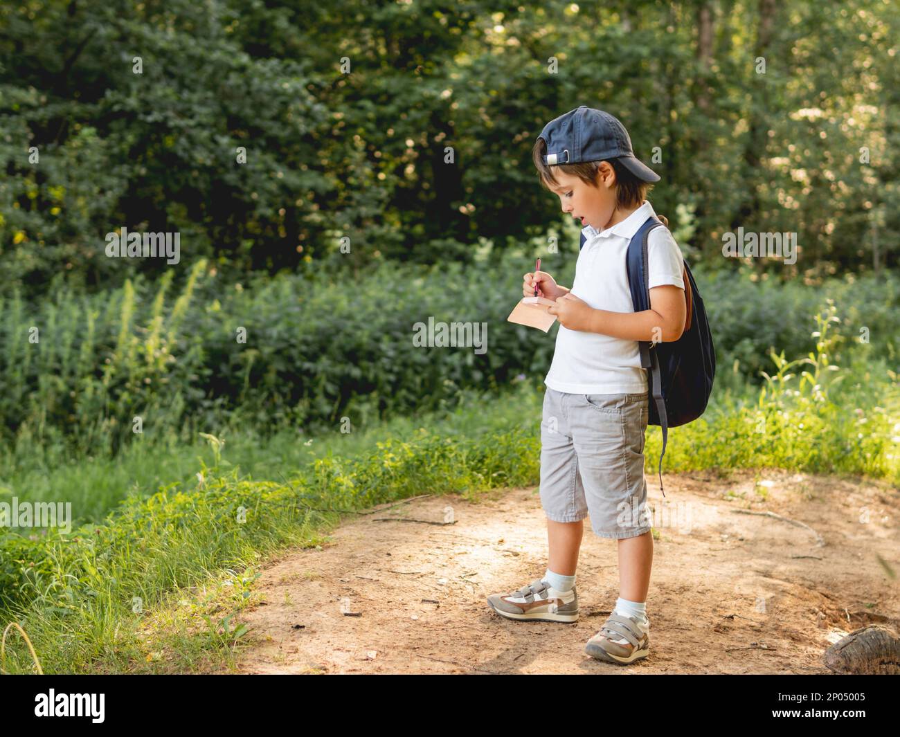 Achtsamer Junge schreibt etwas in Notizbuch, während er im Wald läuft. Erkunden Sie die Natur. Sommer Erholung im Freien. Gesunder Lebensstil. Stockfoto
