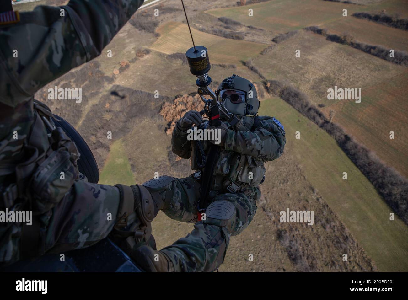 Sgt. 1. Class Anthony Bonillas, ein Soldat der Kosovo Force (KFOR) Regional Command-East (RC-E) mit der medizinischen Evakuierungseinheit, die Charlie Company zugewiesen wurde, 2. Bataillon, 149. Aviation Regiment, bereitet sich darauf vor, auf den Boden abgesenkt zu werden, während er eine Hebeoperation von einem UH-60 Black Hawk Helikopter in Camp Bondsteel durchführt, Kosovo am 6. Januar 2023. Stockfoto