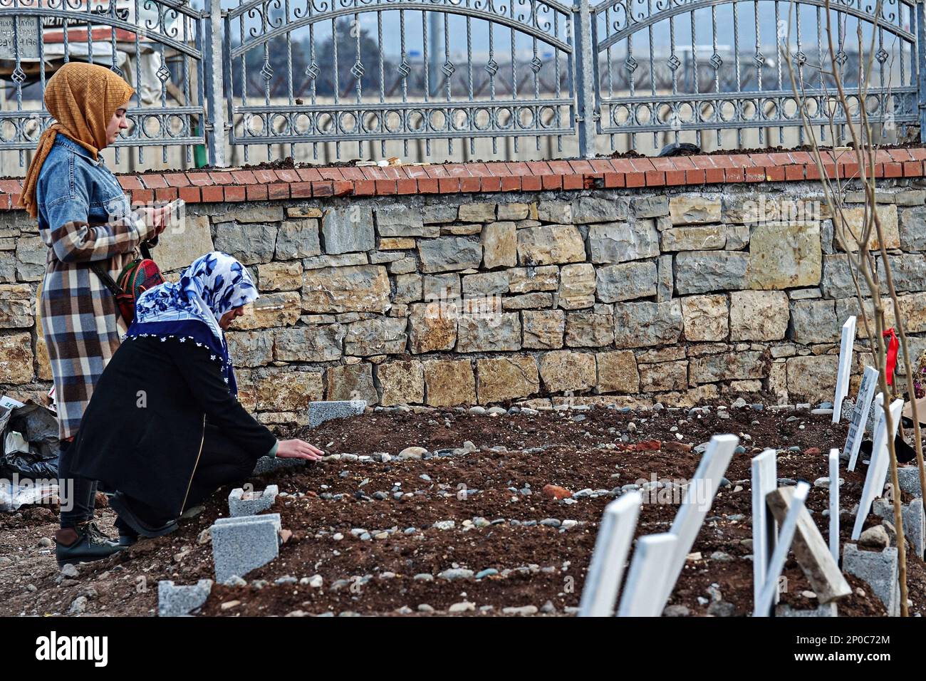 Diyarbakir, Türkei, 02/03/2023, eine junge Frau wird gesehen, wie sie den Koran für ihren Verwandten liest, der bei dem Erdbeben gestorben ist, während ihre Mutter beim Berühren des Grabes weint. Diejenigen, die bei den schweren Erdbeben vom 6. Februar starben und in der Türkei weitergingen, wurden vor Freitag mit Gebeten in ihren Gräbern geehrt, was von Muslimen als heilig angesehen wird. Da die Zahl der Todesopfer in 11 von dem Erdbeben betroffenen Städten hoch war, wurde jeder städtische Friedhof um einen neuen Friedhof erweitert. Die meisten der 414 Menschen, die in 7 Gebäuden starben, die in der Stadt Diyarbak zerstört wurden, wurden in t begraben Stockfoto