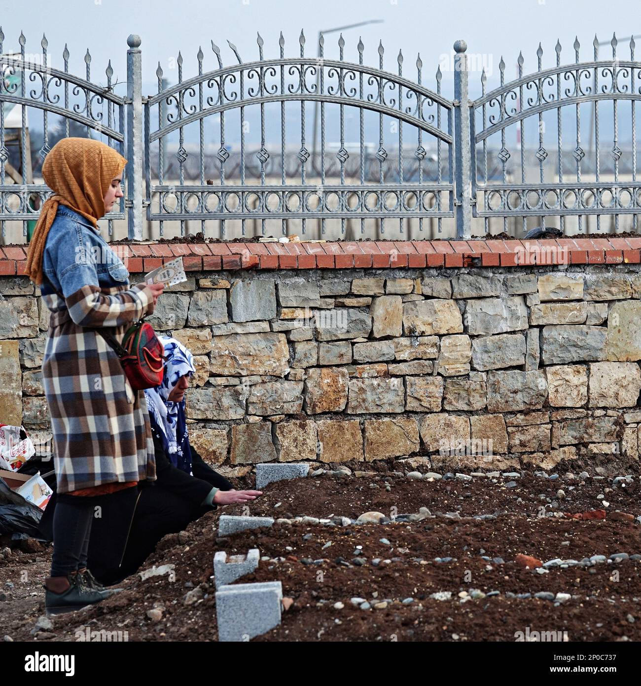 Diyarbakir, Türkei, 02/03/2023, eine junge Frau in Diyarbakir wird gesehen, wie sie den Koran für ihren Verwandten liest, der während des Erdbebens starb, während ihre Mutter weint und betet. Diejenigen, die bei den schweren Erdbeben vom 6. Februar starben und in der Türkei weitergingen, wurden vor Freitag mit Gebeten in ihren Gräbern geehrt, was von Muslimen als heilig angesehen wird. Da die Zahl der Todesopfer in 11 von dem Erdbeben betroffenen Städten hoch war, wurde jeder städtische Friedhof um einen neuen Friedhof erweitert. Die meisten der 414 Menschen, die in 7 Gebäuden starben, die in der Stadt Diyarbak zerstört wurden, wurden im Yenikoy c begraben Stockfoto