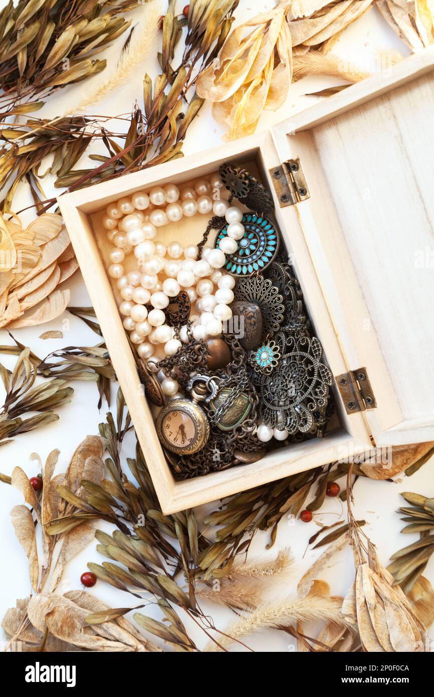 Stapel der alten Vintage Schmuck und eine Taschenuhr in einer Holzkiste. Retro Style Mode Accessoires für Frauen - Halsketten und Perle Perlen Stockfoto