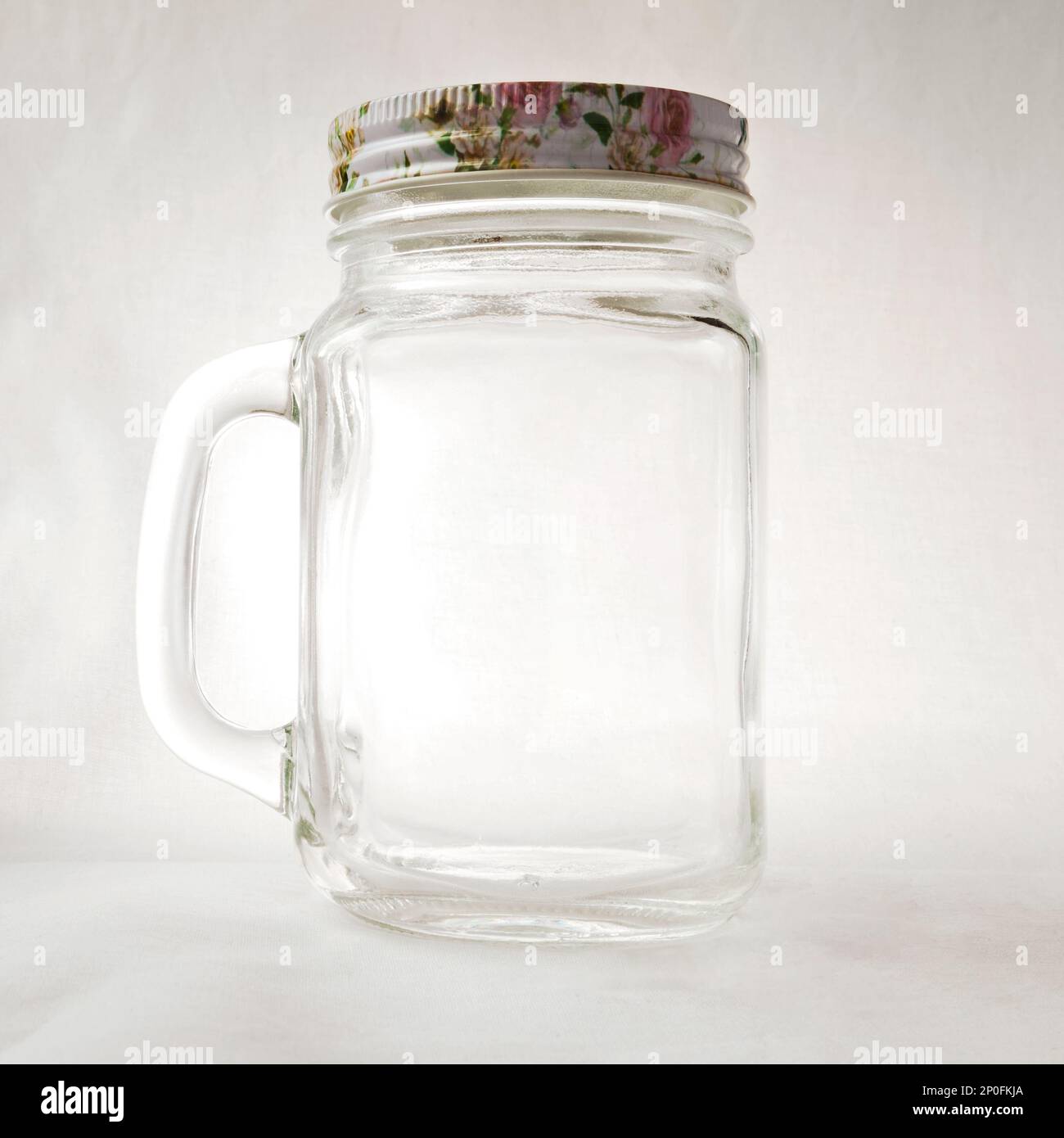 Leeren Sie den durchsichtigen Fassbecher mit einem Griff und einem Deckel auf weißem Hintergrund. Transparenter Glasbecher für sommerliche Drinks aus nächster Nähe Stockfoto