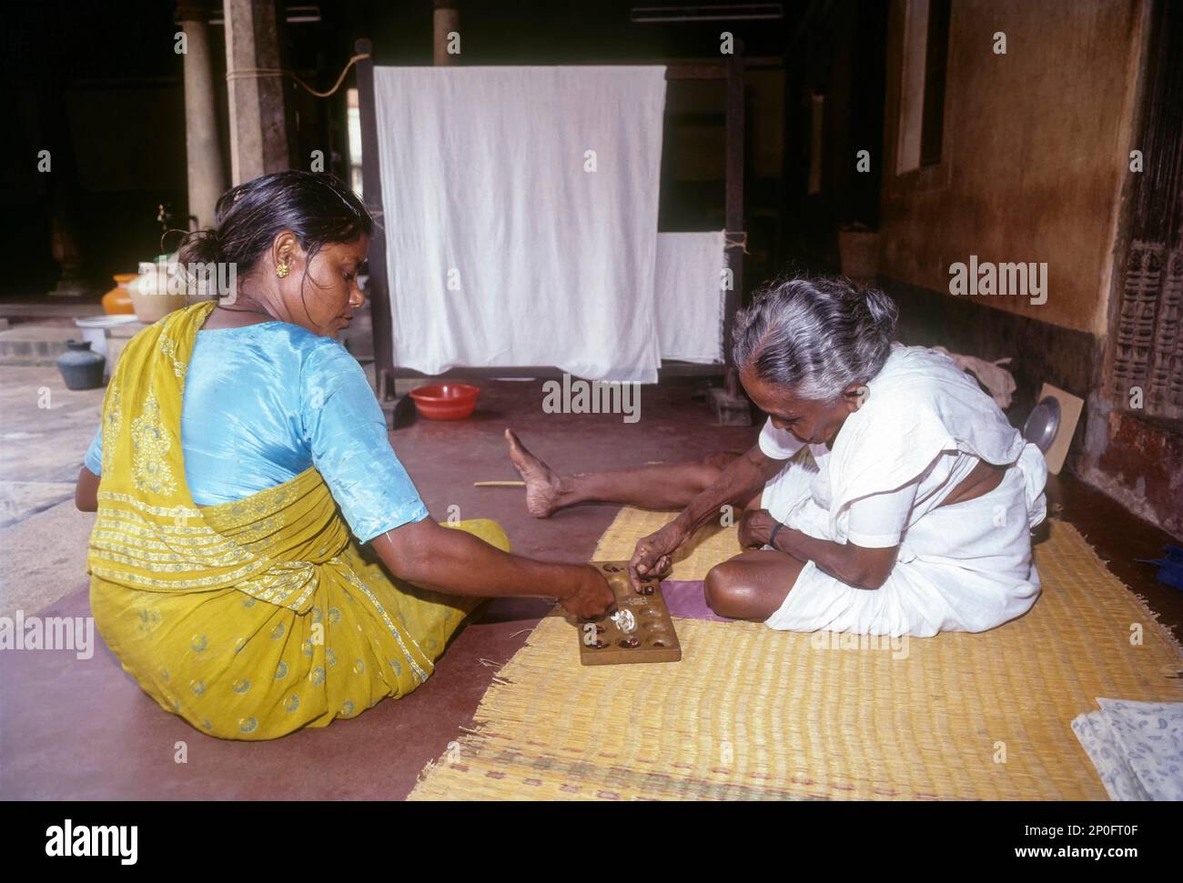 Zwei Frauen, die auf dem Boden saßen und Pallanguzhi spielten in Chettinad, Tamil Nadu, Indien. Pallanguzhi wurde hauptsächlich von Tamilinnen als Zeitvertreib gespielt. Stockfoto