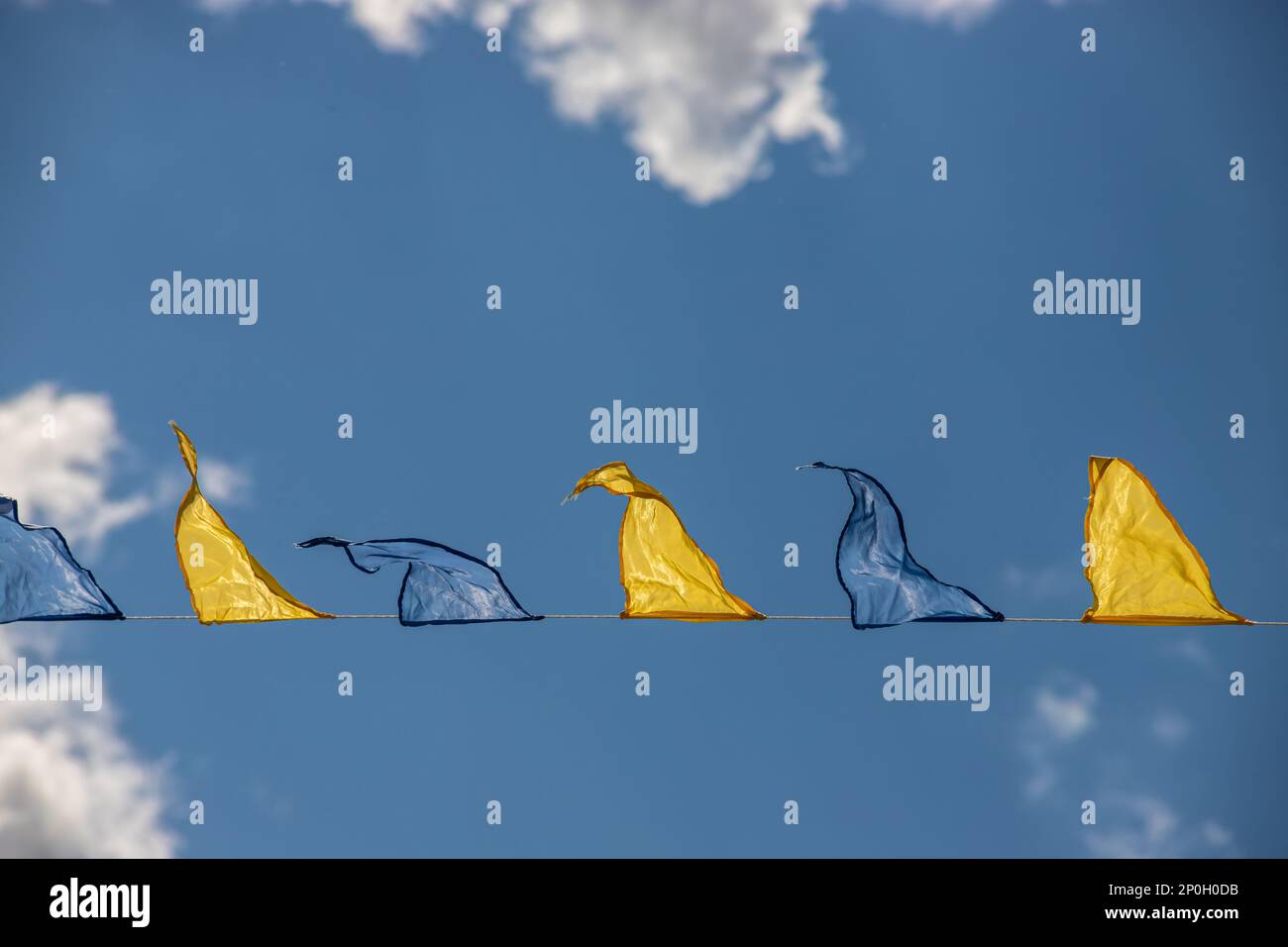 Gelbe und blaue dreieckige Festivalflaggen am Himmel mit weißen Wolken. Feier Im Freien. Festliche Stimmung Stockfoto