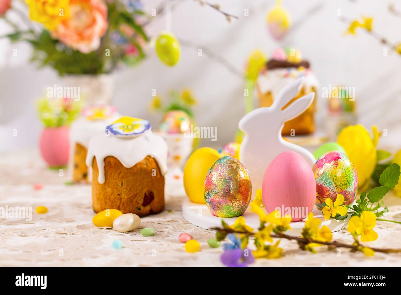 Osterstill mit bunten Osterkuchen, Ostereiern auf Kaninchen-Dessertteller. Traditionelles Ostergeschenk auf festlichem Tisch, dekoriert mit Frühlingsflo Stockfoto