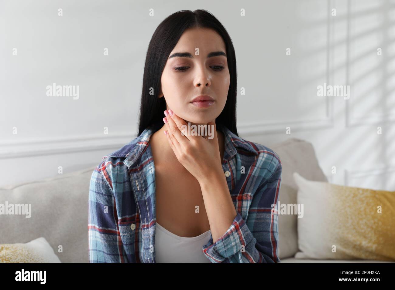 Junge Frau, die zu Hause eine Schilddrüsen-Selbstuntersuchung macht Stockfoto