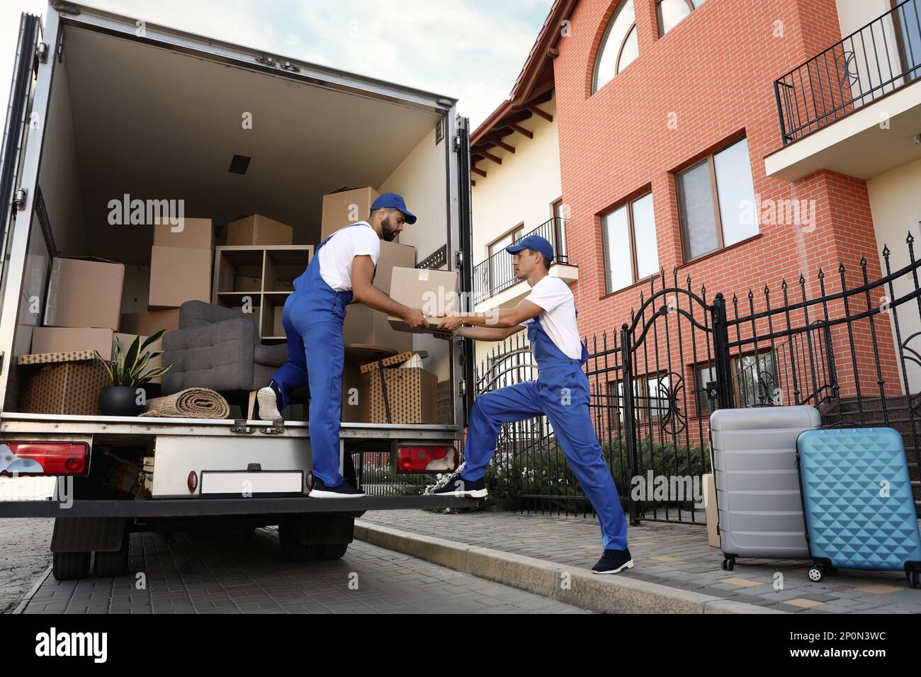 Arbeiter, die Kisten aus dem Lieferwagen im Freien entladen. Umzugsdienst Stockfoto