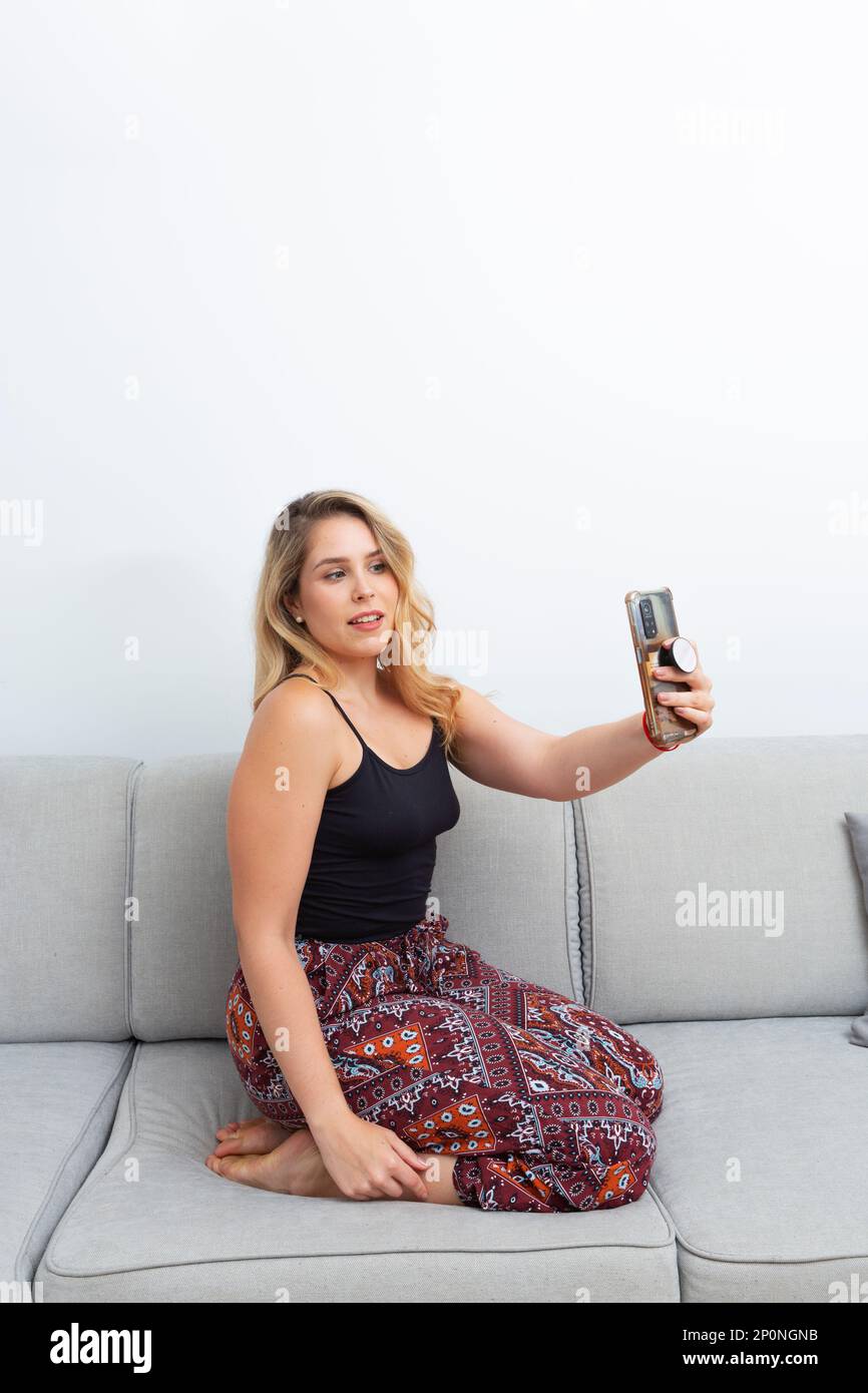 Hübsche blonde Frau, die Fotos mit ihrem Smartphone auf dem Sofa in ihrem Wohnzimmer macht Stockfoto