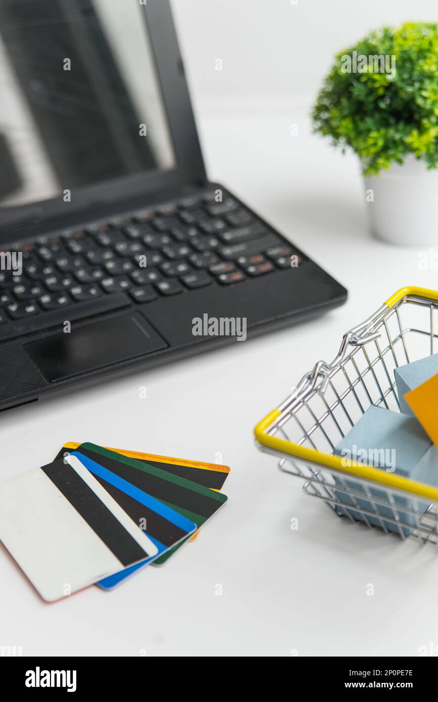 Laptop, grüne Pflanze, Warenkorb und Kreditkarten. Online-Shopping und Lieferkonzept vertikale Foto Stockfoto