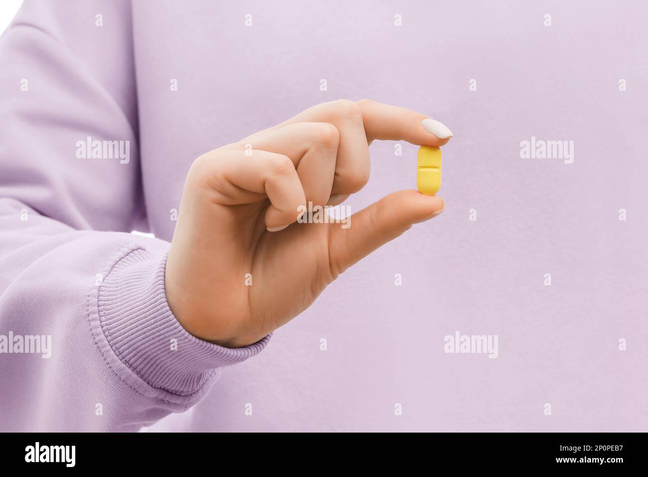 Gekürzte Aufnahme einer Frau in einem übergroßen, lavendelfarbenen Sweatshirt mit einer gelben Pille. Schließen. Stockfoto