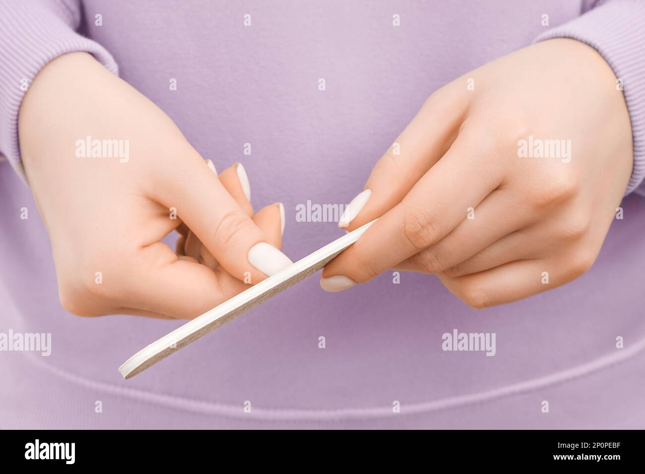 Gekürzte Aufnahme einer Frau in einem übergroßen, lavendelfarbenen Sweatshirt, die ihre Nägel feilte. Schließen. Stockfoto