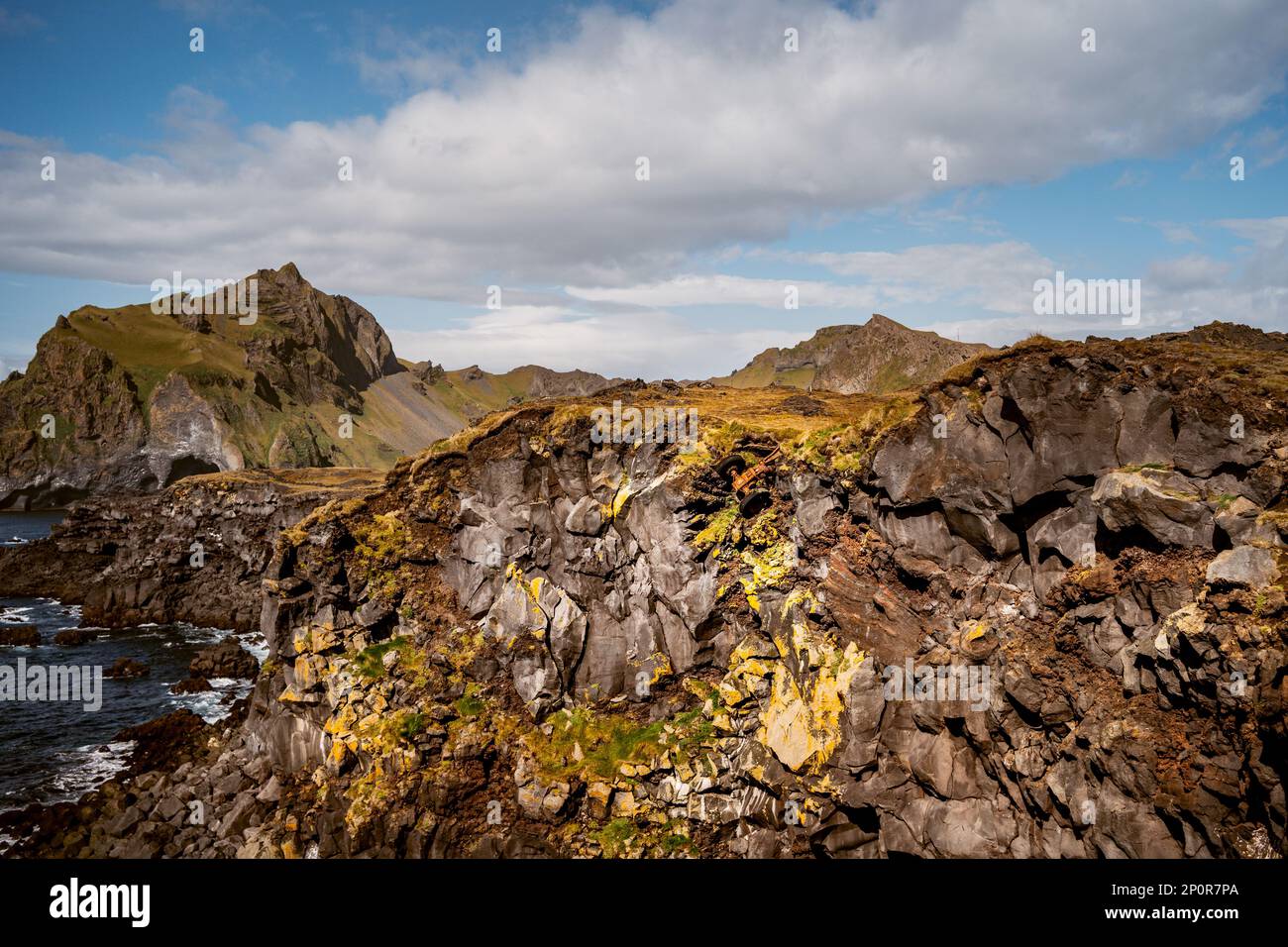 Blick auf Westman Island mit einem orangefarbenen Truck, der über den Klippen hängt, eingebettet in das Unterholz Stockfoto