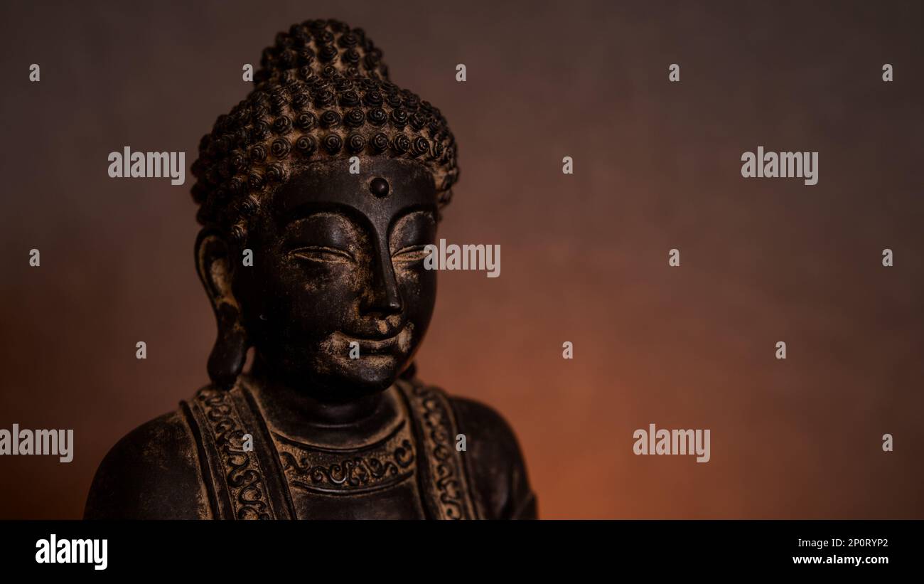 Buddha-Statue aus nächster Nähe in einer dunklen Umgebung mit goldenem Hintergrund und Kerzenlicht. Leerer Bereich für Text auf der rechten Seite Stockfoto