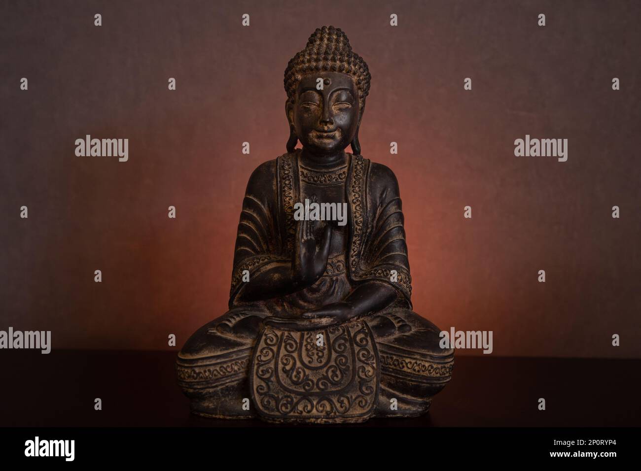 Die Buddha-Statue, die in einer dunklen Umgebung auf einem goldenen, leuchtenden Hintergrund bei Kerzenlicht meditiert Stockfoto