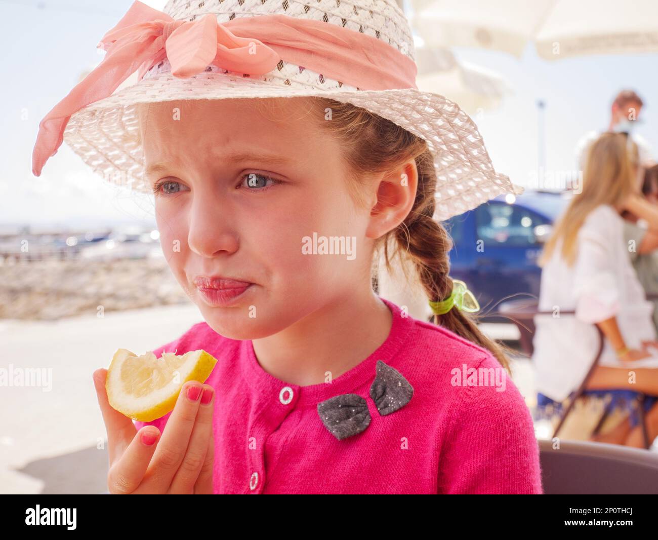 Ein junges Mädchen reißt sich ein Gesicht vom sauren Geschmack eines Zitronenstücks Stockfoto