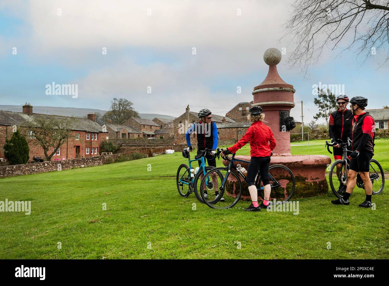 Radfahrer am alten Brunnen auf dem Dorfgrün, mit Dufton Pike dahinter, Dufton, Eden Valley, Cumbria. Wasserbrunnen gebaut von London Lead Co Stockfoto