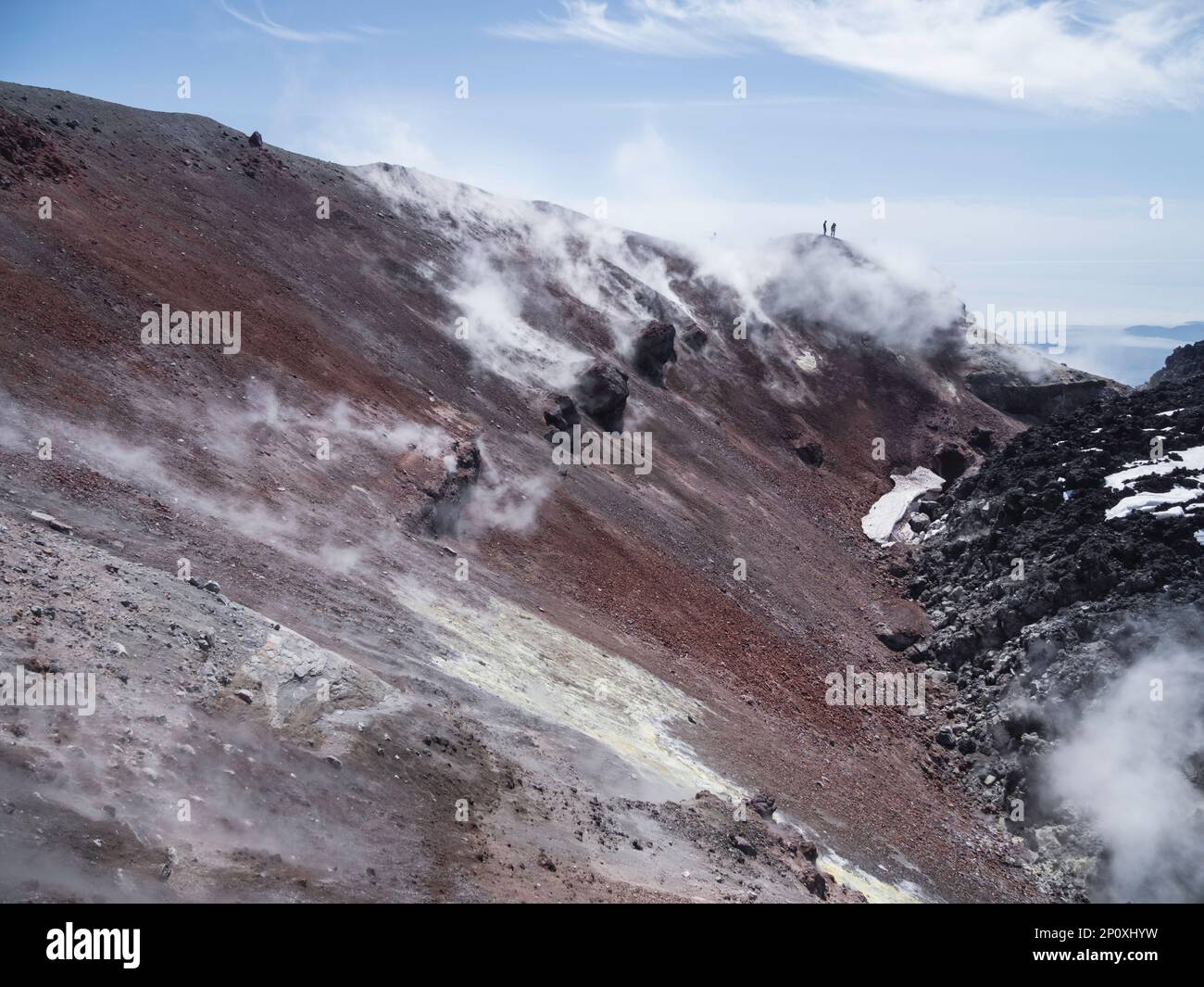 Silhouette von Männern beim Wandern in der Caldera des Stratovulkans Avachinsky, auch bekannt als Vulkan Avacha. Rucksacktouristen bewegen sich auf Felsen hinter Dampf von Stockfoto