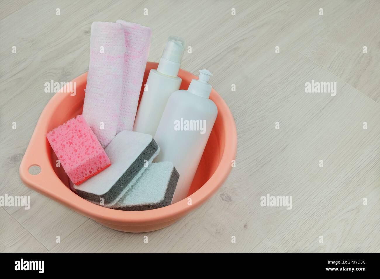 Reinigungskonzept. Waschmittelflaschen mit Waschlappen für die allgemeine Ordnung und Sauberkeit in einem pinkfarbenen Waschbecken auf Holzhintergrund. Speicherplatz kopieren. Stockfoto
