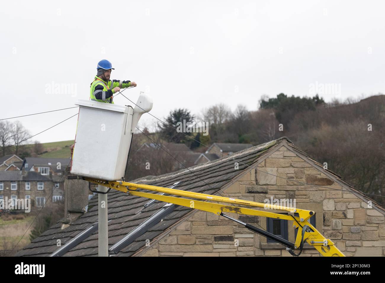 Telekommunikationsunternehmen mit entsprechender Sicherheitsausrüstung, das von einem Kirschpflücker aus arbeitet, um eine neue private Telefonleitung in West Yorkshire, Großbritannien, zu installieren Stockfoto