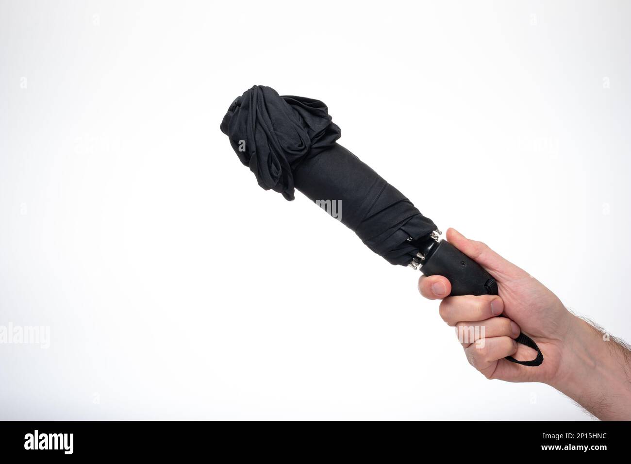 Gefalteter und geschlossener schwarzer Regenschirm aus Stoff, der vom Menschen in der Hand gehalten wird. Nahaufnahme des Studios, isoliert auf weißem Hintergrund. Stockfoto