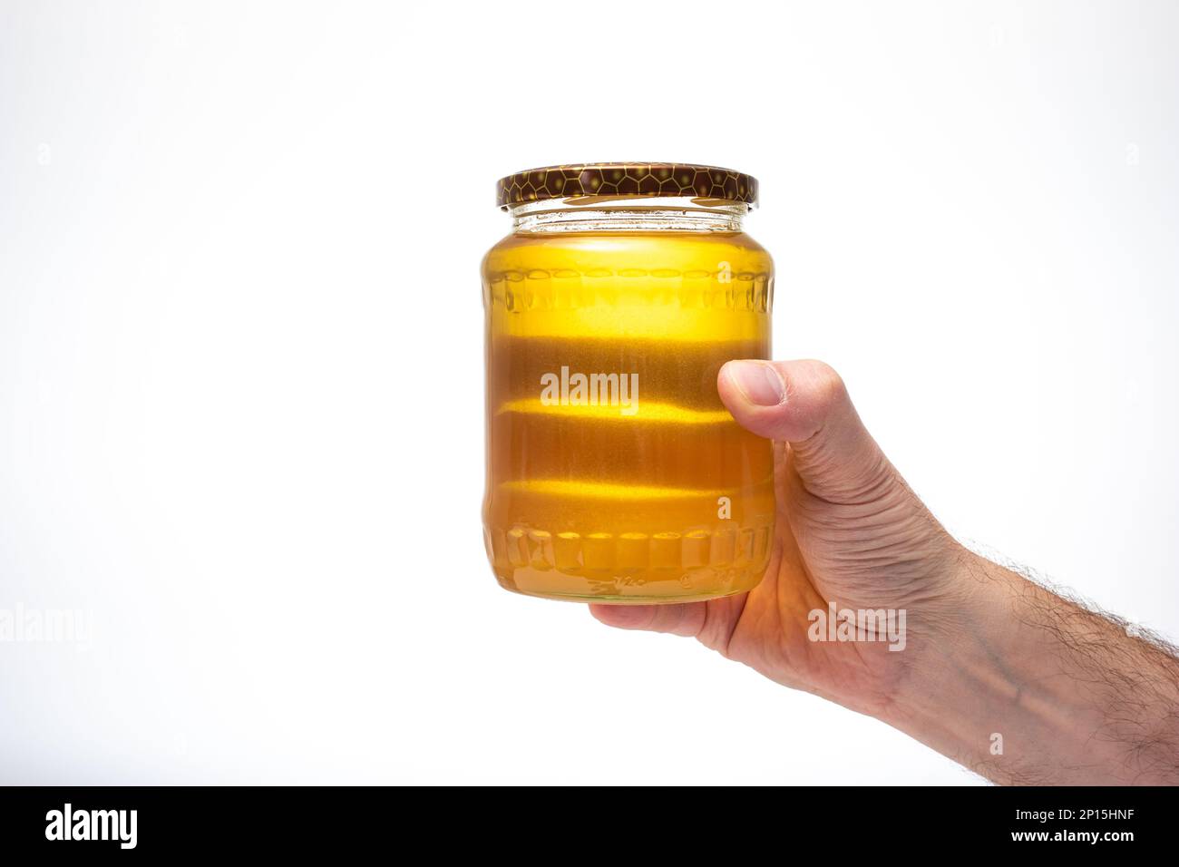 Frischer goldgelber Bienenhonig in einem Glasgefäß, gehalten von weißer männlicher Hand. Nahaufnahme des Studios, isoliert auf weißem Hintergrund. Stockfoto