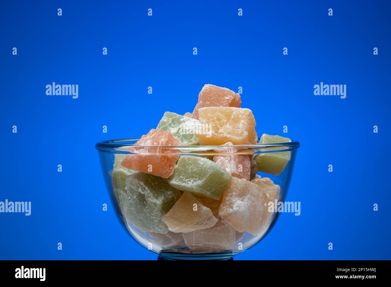 Würfel mit bunten türkischen Köstlichkeiten in einer Glasschüssel. Nahaufnahme des Studios, isoliert auf blauem Hintergrund. Stockfoto