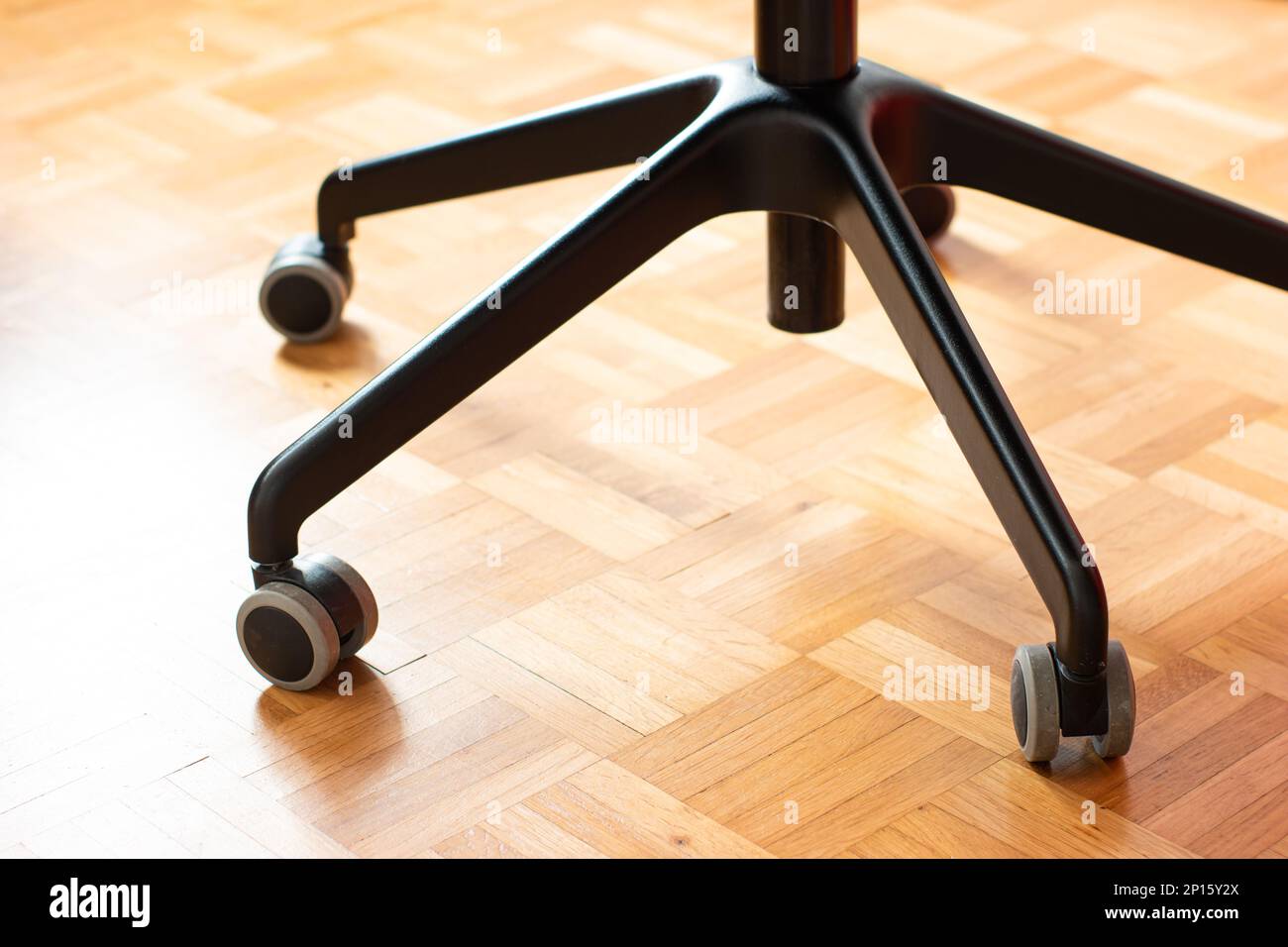 Schwarzer Bürostuhl aus Metall mit drehbaren Rädern auf Holzfußboden, geringe Tiefenschärfe, niemand. Stockfoto