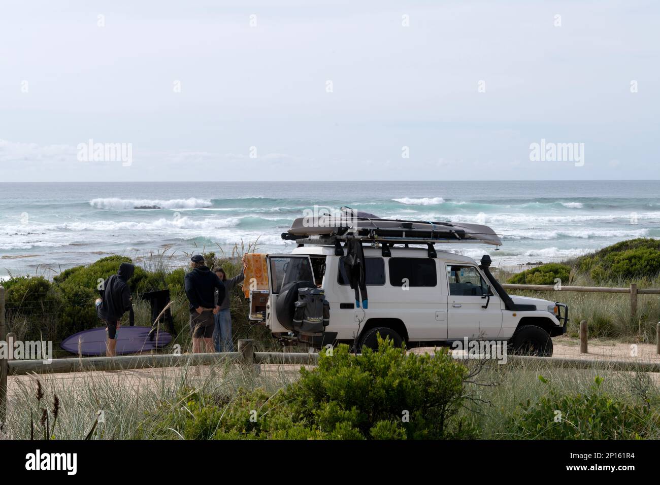 Roadtrip. Surf-Van und Crew auf der Straße reisen mit Surf-, Angel- und Campingausrüstung und Breaking Surf im Hintergrund, Shelly Beach, Tasmanien Stockfoto