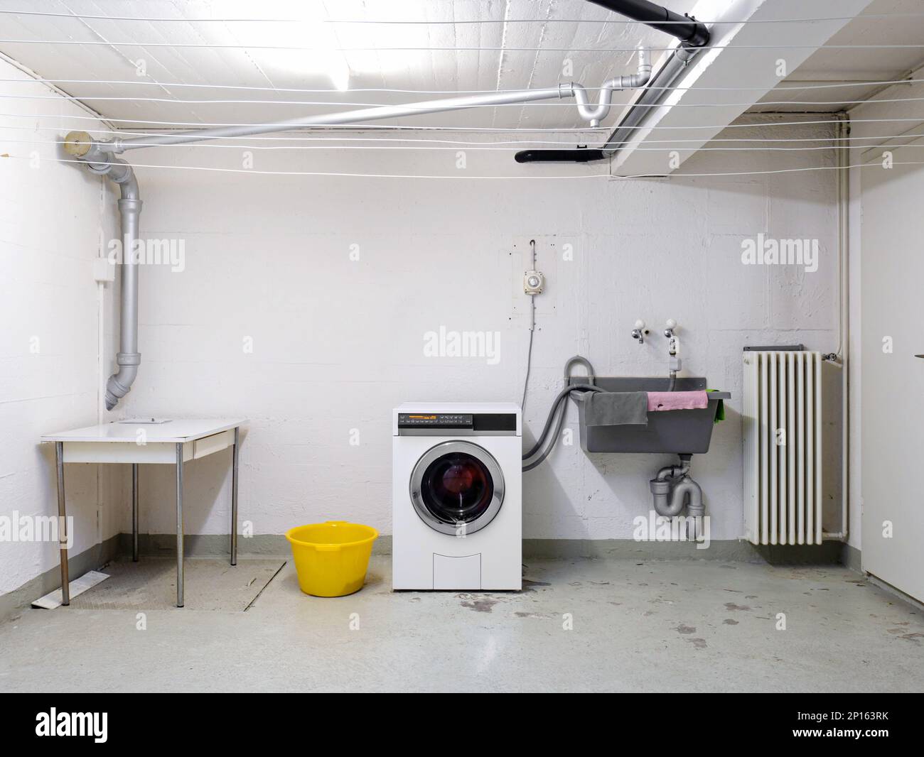 Gemeinschaftswohnungsgebäude Waschraum mit Waschmaschine in gebrauchtem Waschbecken und Rohrleitungen Weitwinkelblick. Stockfoto