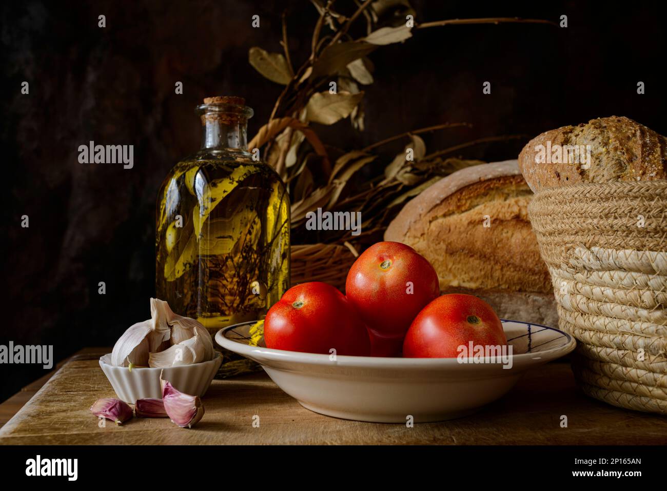Klassisches Stillleben mit extra nativem Olivenöl, Tomaten, Knoblauch und Brot. Zutaten eines typischen Frühstücks der mediterranen Diät. Stockfoto