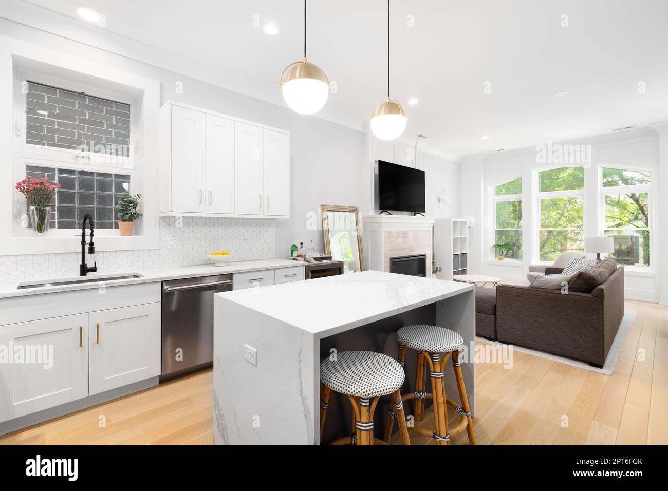 Eine luxuriöse weiße Küche mit goldenen Lichtern und Blick auf ein gemütliches Wohnzimmer. Stockfoto