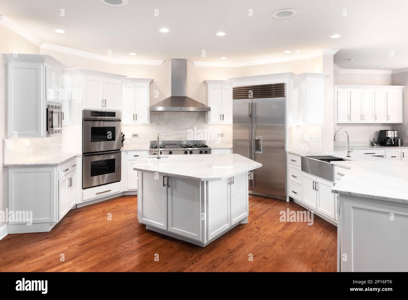 Eine große, luxuriöse Küche mit weißen Schränken, Edelstahlgeräten und Hartholzböden. Stockfoto