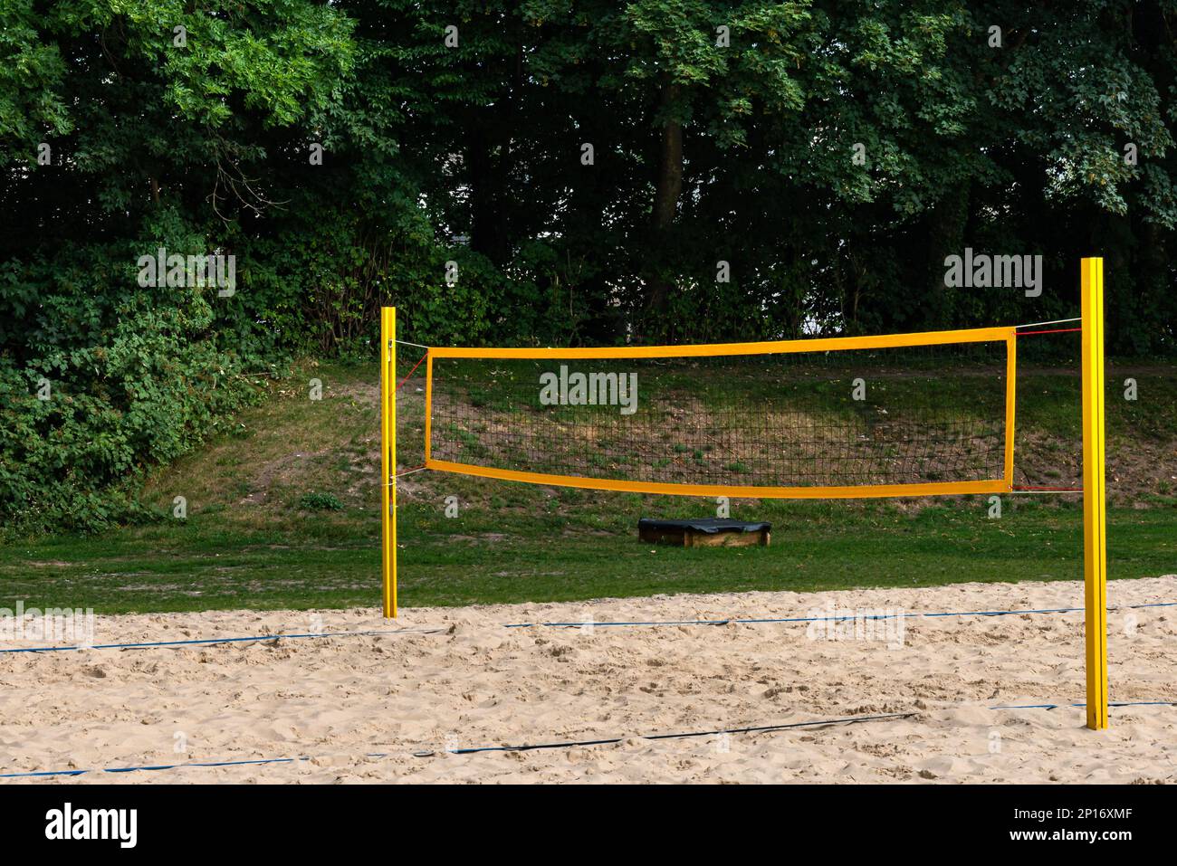 Spielplatz für Beachvolleyball mit hellgelbem Netz. Grüne Bäume im Hintergrund Stockfoto