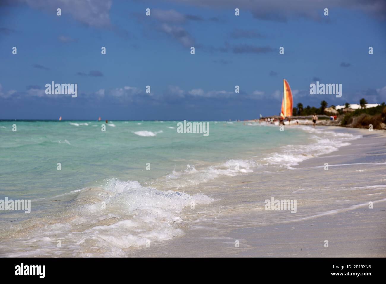 Blick von den Meereswellen bis hin zu Segelbooten und schwimmenden Menschen. Wassersport und Urlaub an einem Strand karibischer Inseln Stockfoto