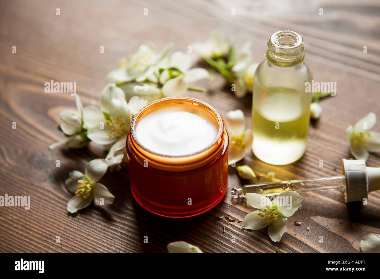 Gesichtscreme aus biologischem Anbau mit Ölflasche, Jasminblütenöl und Sahne auf Holzhintergrund Stockfoto