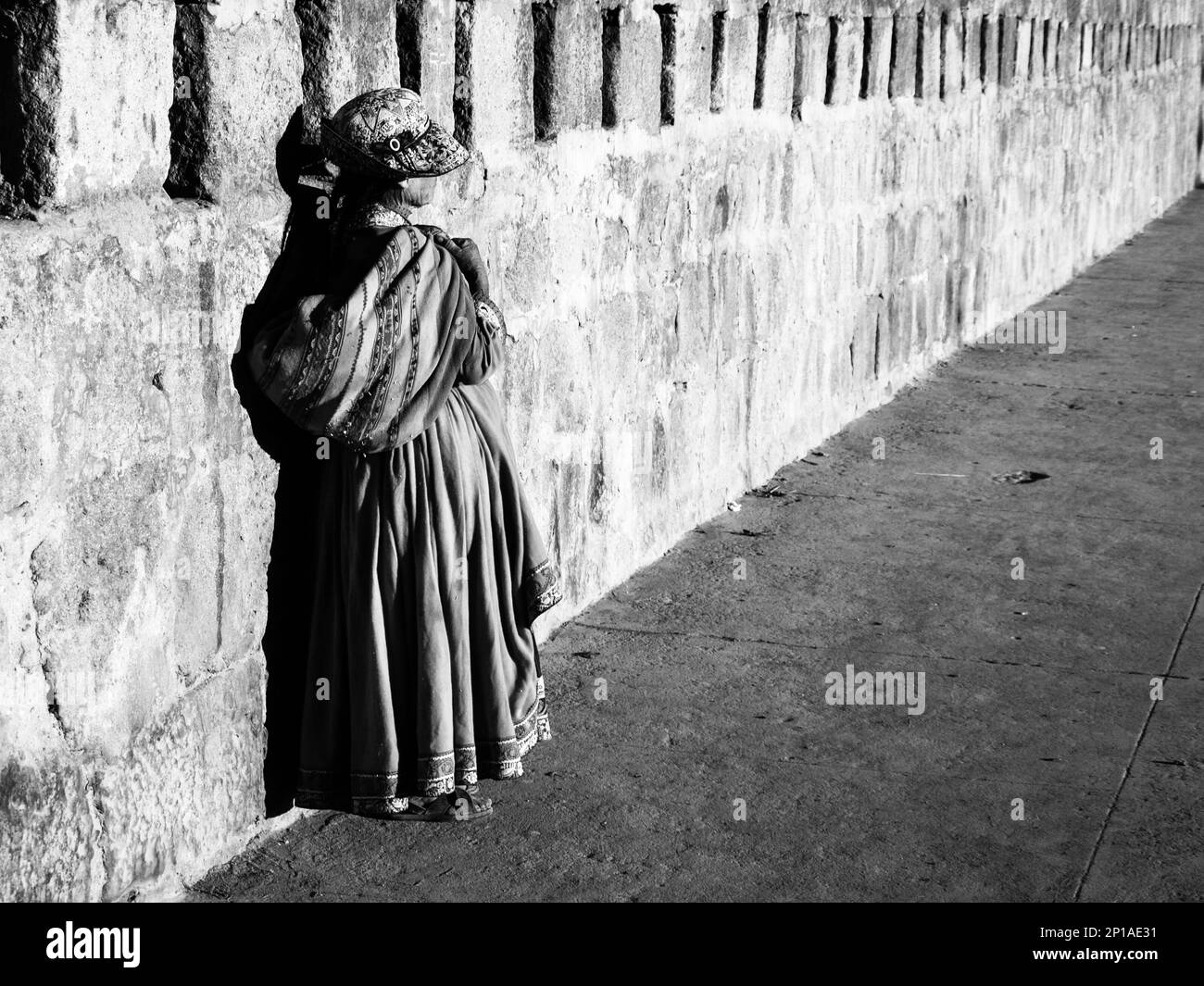 Paruanische Frau in traditionellem Kleid mit Rock, Tasche und Hut, die an der Wand stehen. Schwarzweißbild. Stockfoto