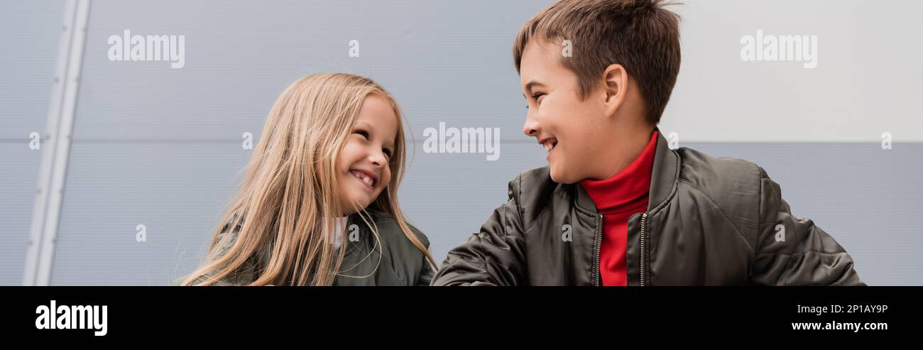 Glückliche Kinder in Bomberjacken, die sich anschauen, während sie in der Nähe des Einkaufszentrums stehen, Banner, Stock Image Stockfoto