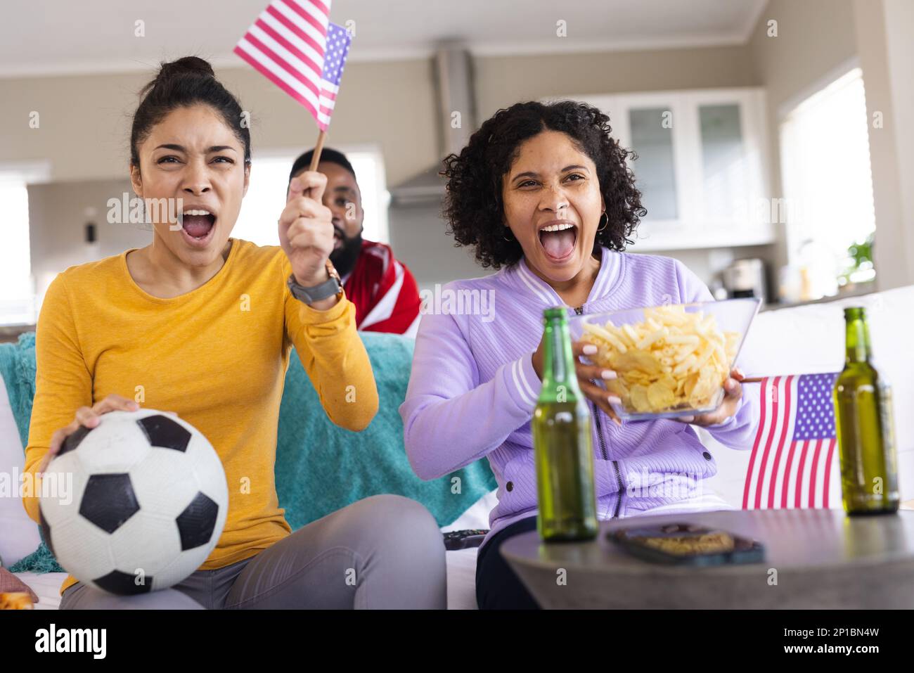 Glückliche, vielfältige Freunde sitzen auf dem Sofa, sehen sich das Fußballspiel an und unterstützen Stockfoto