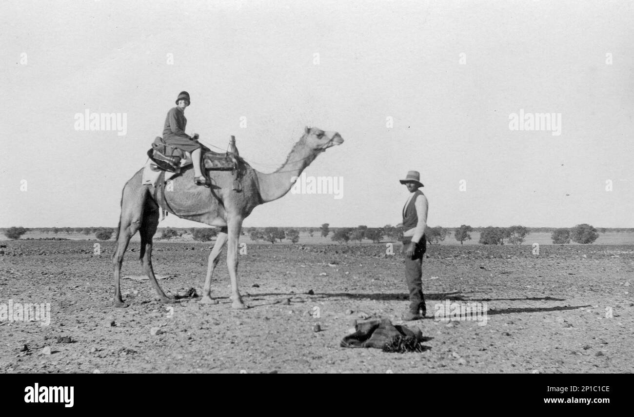 Schwester W. Grimison von der Australian Inland Mission sitzt auf einem Kamel, Birdsville, Queensland; Australien, 1927, Mit Norman Rummel neben dem Kamel. Die Australian Inland Mission richtete ab 1912 15 Pflegeheime/Buschkrankenhäuser an abgelegenen australischen Standorten ein. Stockfoto