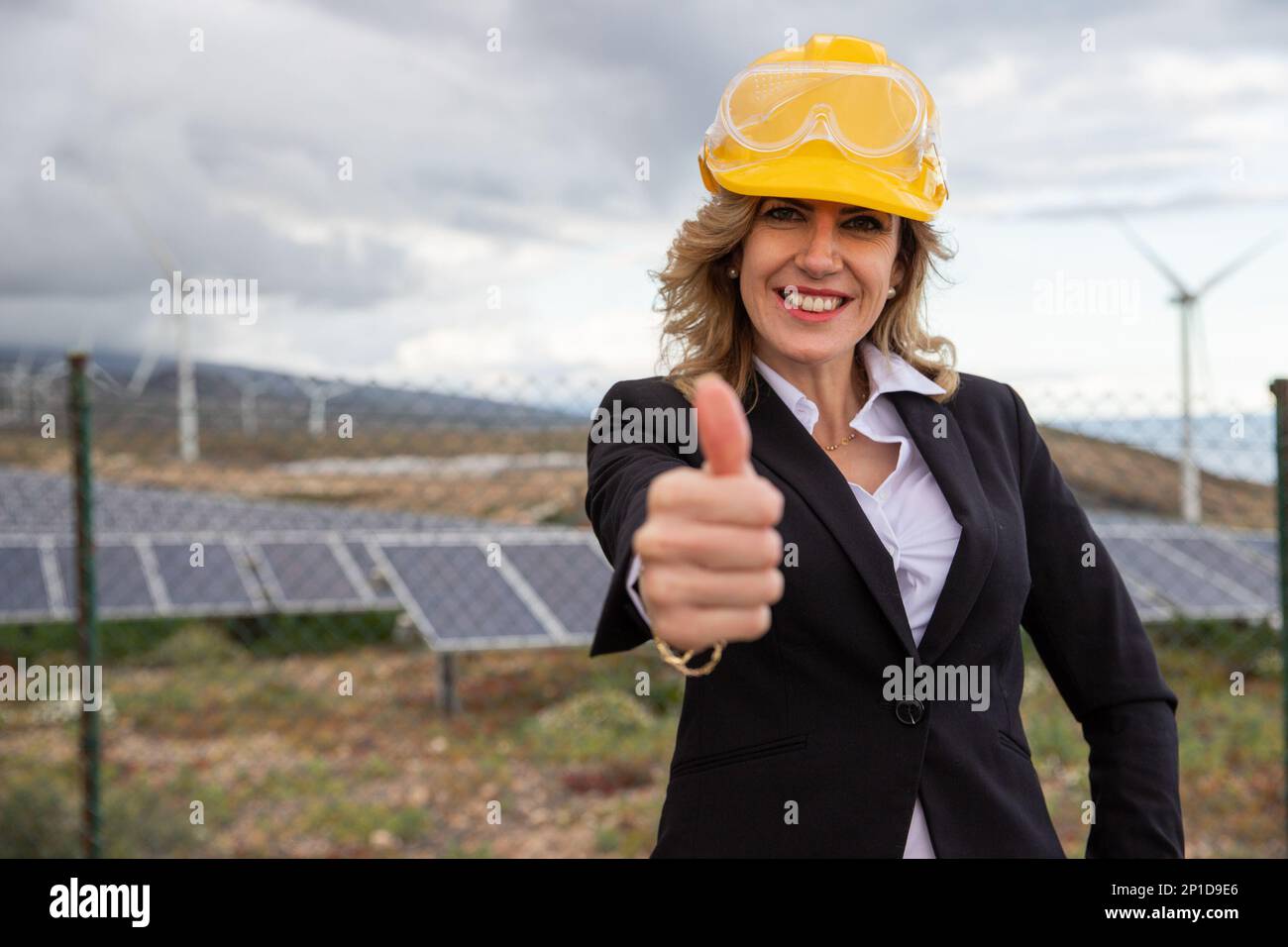 Eine erfolgreiche Ingenieurin, die einem Solarkraftwerk den Daumen nach oben zeigt. Stockfoto