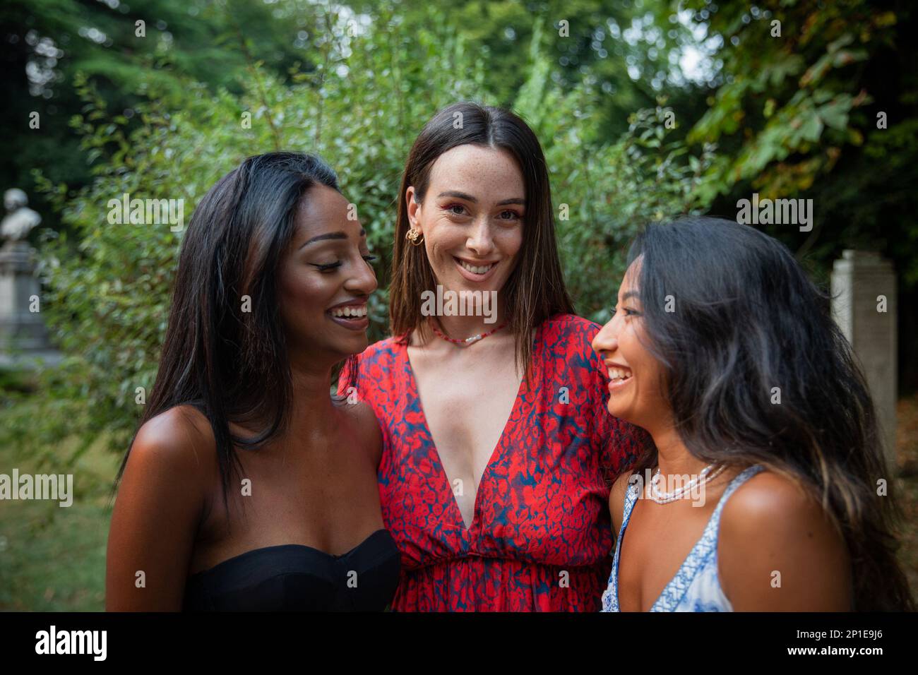 Drei Freundinnen unterschiedlicher ethnischer Herkunft lachen in einem öffentlichen Park zusammen. Stockfoto