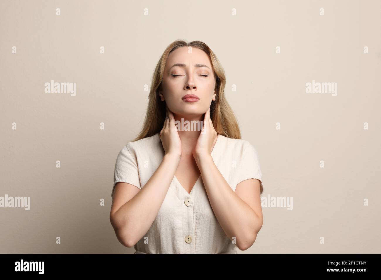 Junge Frau, die Schilddrüsen-Selbstuntersuchung auf beigefarbenem Hintergrund macht Stockfoto
