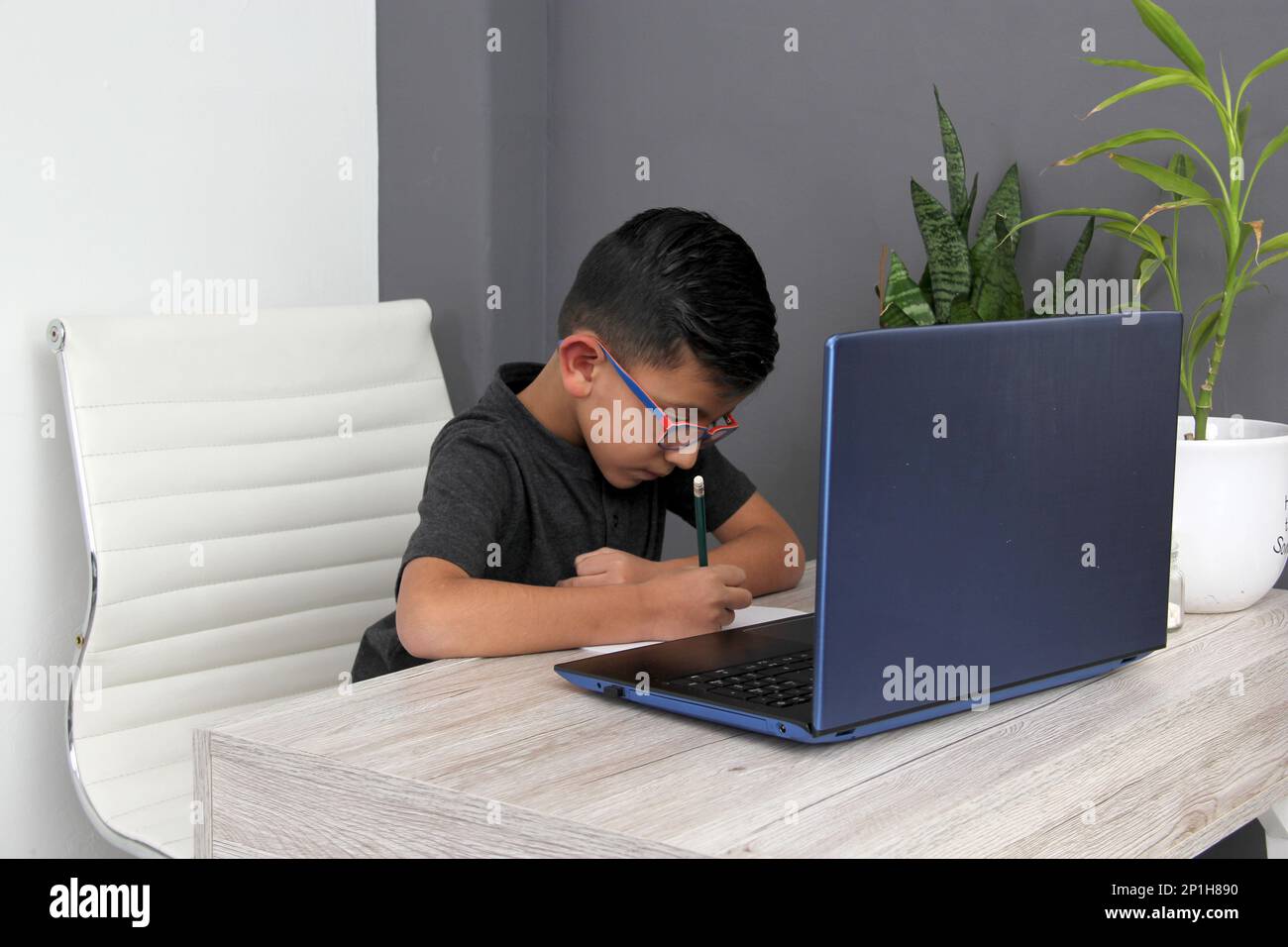 Ein 7-jähriger Latino-Junge mit Brille, der zu Hause zu Hause an Online-Kursen teilnimmt, ist überrascht, dass er mit einem Laptop und dem Studium an einem Tisch sitzt Stockfoto