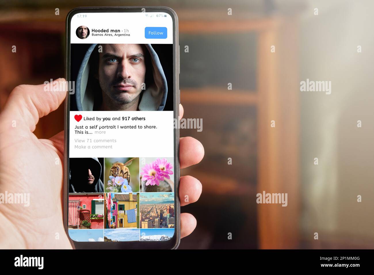 Ein Mann, der ein Mobiltelefon mit einer App-Schnittstelle für soziale Medien auf dem Bildschirm hält, zeigt das Profil eines jungen erwachsenen Influencer man mit einem Foto, das auch von ihm geteilt wird Stockfoto