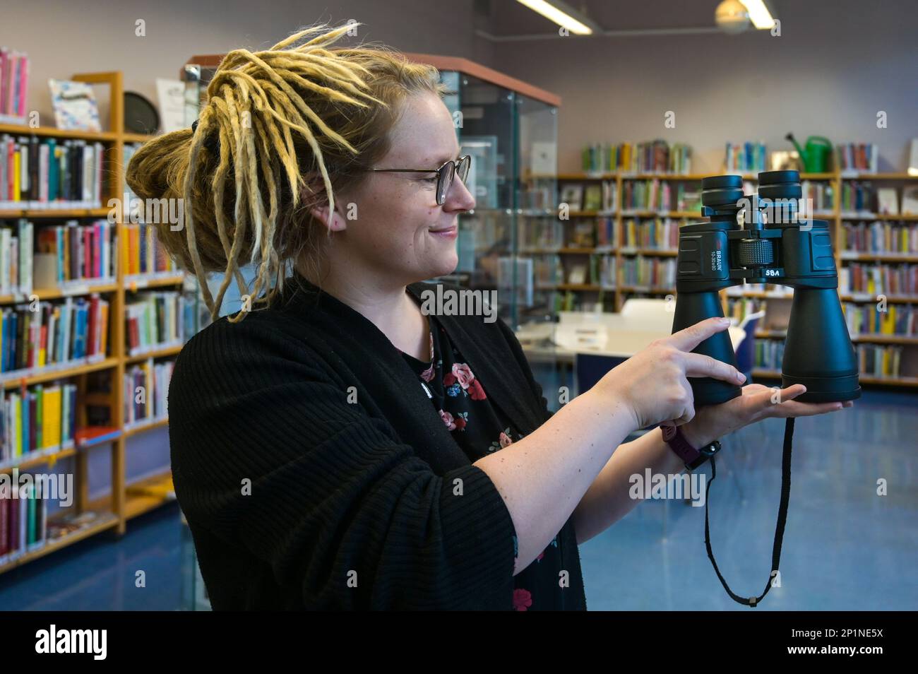 02. März 2023, Sachsen-Anhalt, Halle (Saale): Bibliotheksangestellte Sara Schumann zeigt ein Fernglas, das oft ausgeliehen wird. In der Stadtbibliothek Halle (Saale) können neben viel Literatur auch Gegenstände in einer „Bibliothek der Dinge“ ausgeliehen werden. Das sind Dinge, die nicht immer benutzt werden. Um Kosten zu sparen und die Umwelt zu schützen, müssen diese Artikel nicht von jedem gekauft werden, sondern können für einen Zeitraum von vier Wochen ausgeliehen werden. Foto: Heiko Rebsch/dpa Stockfoto