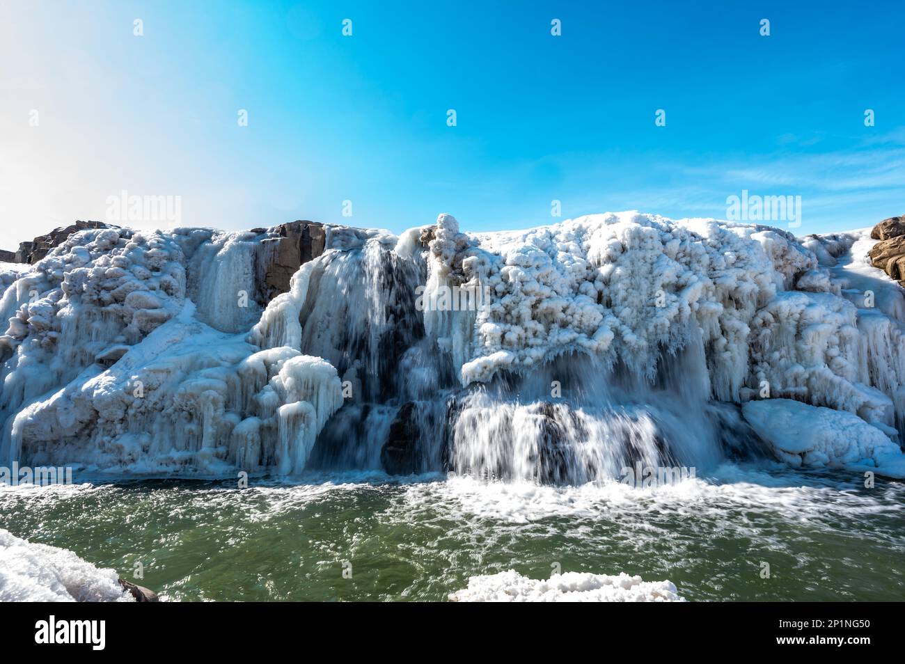 Sioux Falls Park Wasserfall mit Eis und Schnee. Kaskadierendes Schneeschmelzwasser, das über die Oberseite in einen Pool aus stehendem Wasser fließt. Stockfoto