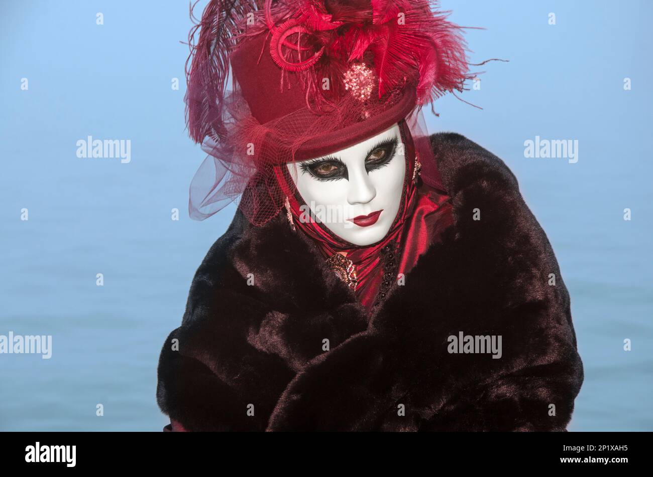 Person mit wunderschönen Augen mit rot-weißer venezianischer Maske mit Lagunenhintergrund in Venedig Stockfoto