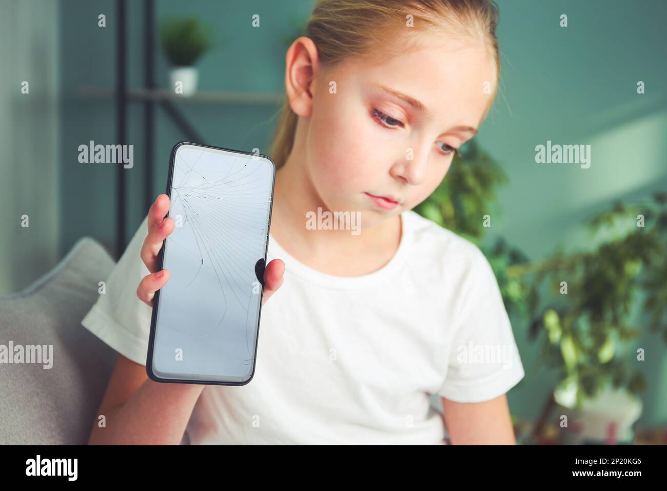 Ein trauriges Mädchen sitzt mit einem kaputten Handy. Der Hauptfokus liegt auf dem Telefonbildschirm. Getöntes Bild. Stockfoto