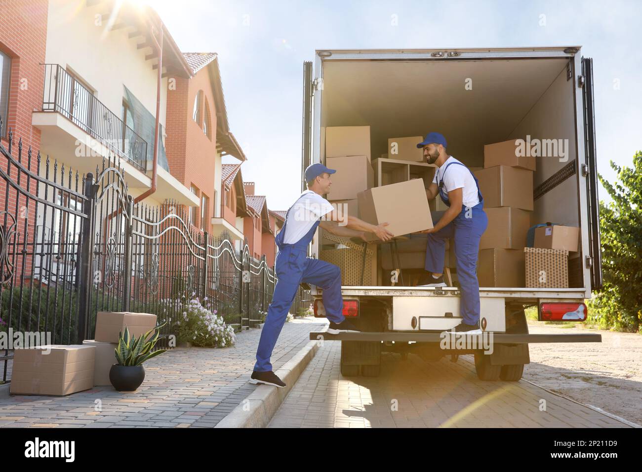Arbeiter, die Kisten aus dem Lieferwagen im Freien entladen. Umzugsdienst Stockfoto